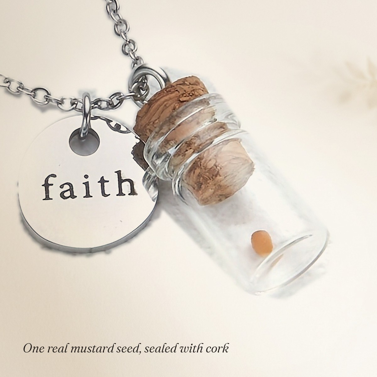 Close-up of a corked glass vial holding one mustard seed, with a small round charm stamped faith